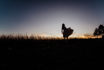 Silhouette girl wearing dress standing on field against sky during sunset