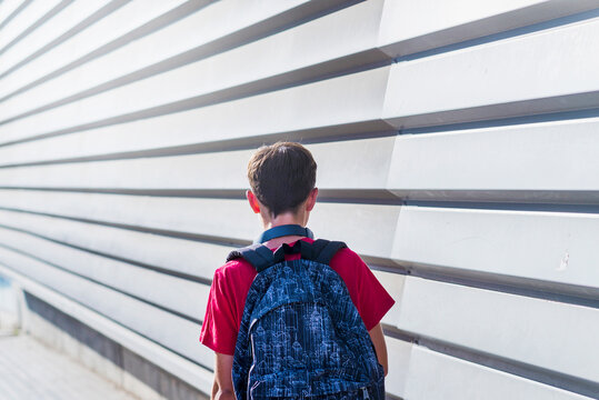 Rear view of schoolboy with backpack walking by wall