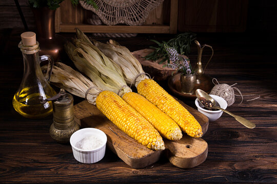 Baked and grilled cobs of corn on wooden cutting board