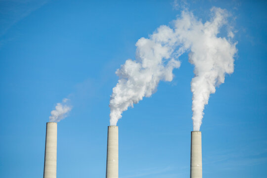 Low angle view of smoke emitting from chimneys against clear blue sky