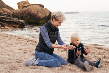 Happy family, friends forever concept. Smiling mother and little son playing together near sea in autumn time