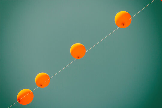Low angle view of orange balloons hanging on wire against clear blue sky during sunny day
