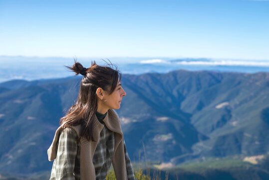 Woman looking at view while sitting on mountain against clear blue sky during sunny day