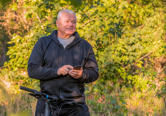 an elderly sports man uses a smartphone while walking on a bicycle