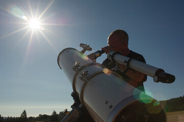 Low angle view of astronomer looking bright sun through telescope against clear sky during sunny day