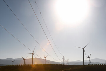 Windmills and electricity pylons on field against clear sky during sunny day