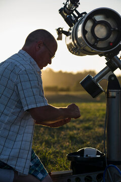 Side view of astronomer standing by telescope on grassy field against clear sky during sunset