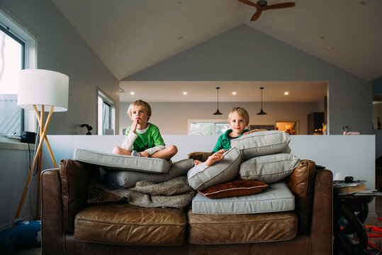 Low angle view of cute brothers watching TV while sitting on stacked cushions at home