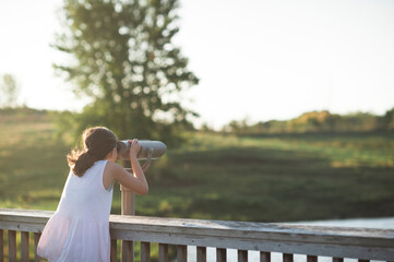 Preteen girl looks into grassy field through viewing scope
