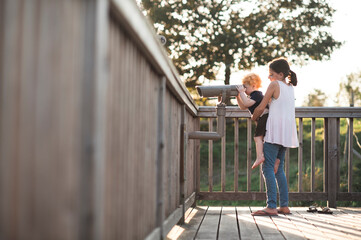 Big sister holds little brother up to look through binoculars