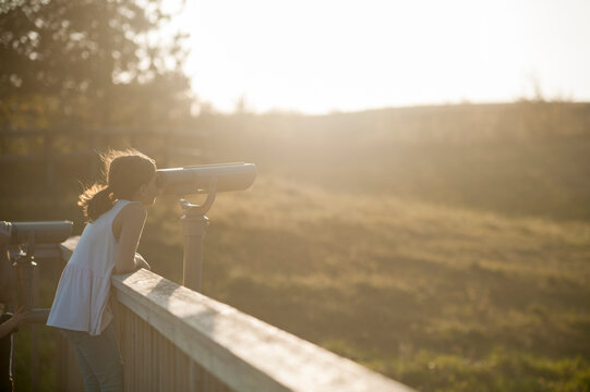 Girl looks through binoculars at a park in hazy summer light