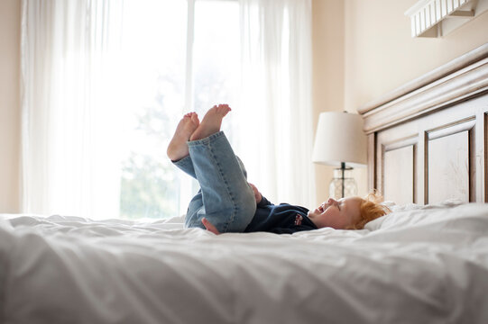 Baby Boy Giggling On Bed In Bedroom With Feet Up In The Air