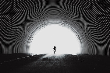 Rear view of silhouette boy riding bicycle in tunnel