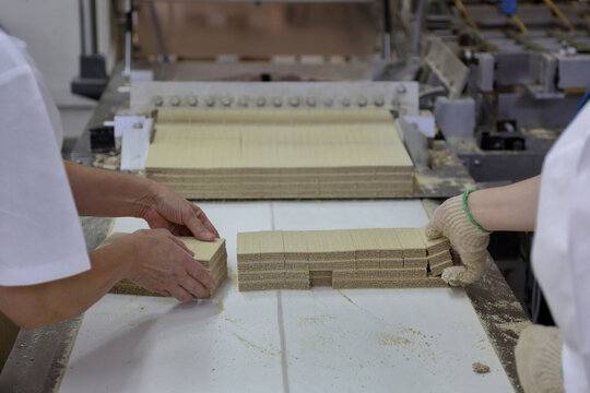 Cropped hands female bakers stacking biscuits on conveyor belt in factory