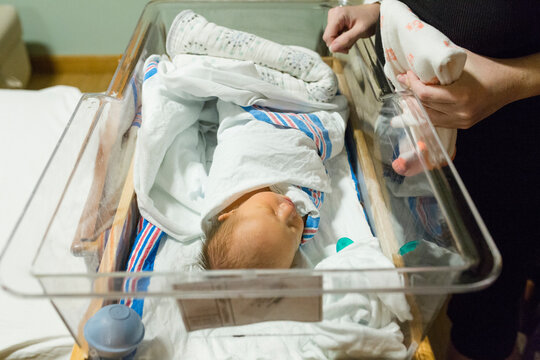 Newborn baby with mom in hospital room wrapped in blanket in bassinet