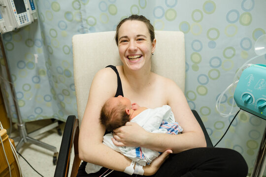 Mother laughs as she holds newborn baby girl in her arms in hospital