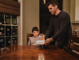 Young boy smiling as dad puts his birthday cake in front of him.