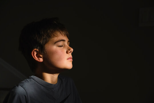 Close up of adolescent boy's face in patch of sun with his eyes closed