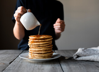 Cropped shot of a child pouring maple syrup on big stack of pancakes.