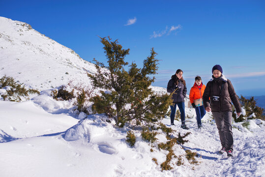 Three people walking on snow covered mountain in a sunny day