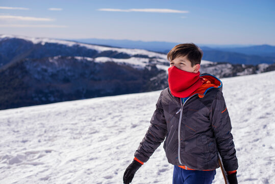 Side view of young boy wearing warm clothes while walking on snow hill