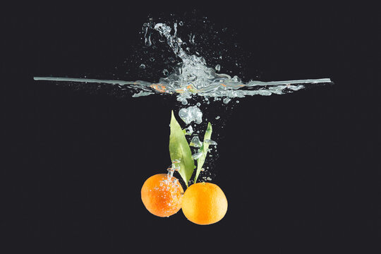 Mandarins with leaves thrown into water on dark background
