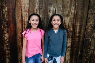 Twin sisters pose for a portrait in front of wooden background