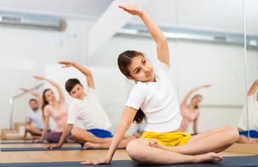 Cute tween girl with brother and parents exercising Hatha yoga in modern yoga studio, doing...
