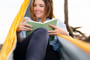 Woman reading a book while relaxing in a hammock along the coast.