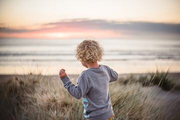Boy with long curly hair running to the beach at sunrise