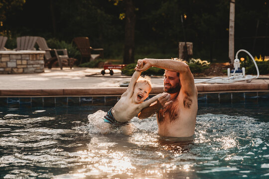 Dad swinging young boy around by arms in pool