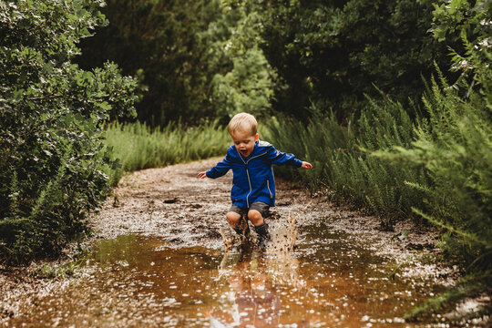 Young boy jumping into muddy puddle and making a splash