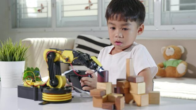Happy Asian little kid boy using remote control playing robotic machine arm for pick up wood block, Funny child learning successful getting lesson control robot arm, Technology science education