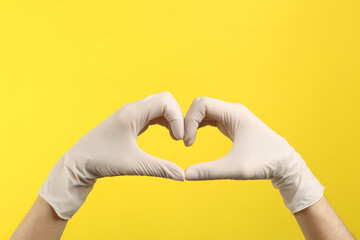 Person in medical gloves showing heart gesture on yellow background, closeup of hands