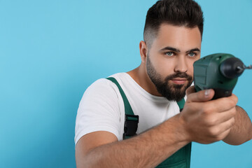 Young worker in uniform with power drill on light blue background. Space for text