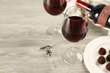 Glasses and bottle of red wine with chocolate candies on white wooden table. Space for text