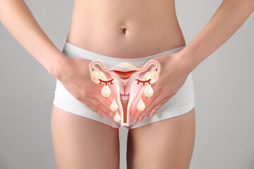 Woman holding hands on her belly and illustration of female reproductive system against light grey...