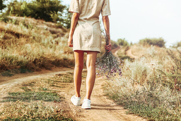 A girl with a bouquet of autumn flowers walks along an autumn road with her back to the camera. Autumn landscape