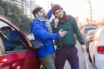 Happy gay couple listening music from mobile by sharing headphones and dancing next to red car in the city. LGBTQ people life. Copy space.