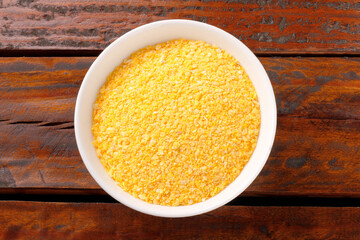 Raw cornmeal flour used in polenta, in ceramic bowl over rustic wooden table