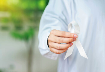 The man in white shirt show white ribbon on out of focus background .