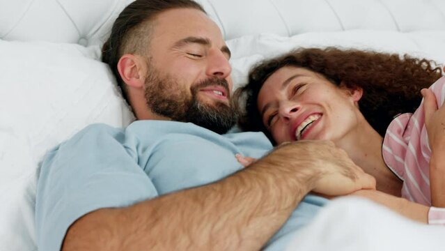 Love, relax and comic couple in bed together in the morning in bedroom, house or home. Smile, happiness and romance of funny happy man and woman cuddle while laughing at a joke, silly or playful.