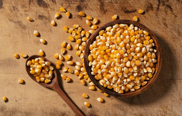 Dried corn kernels and wooden spoon in wooden bowl placed on wooden background.