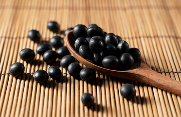 Black soybeans and wooden spoon placed on bamboo background.