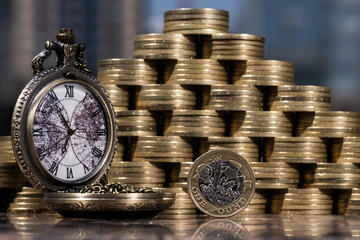 1 English pound coin next to other  coins and an antique stylized pocket watch 