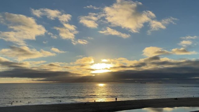 close up of sun rays and clouds and huge reflexion on water of ocean. Cascais, Portugal. some people walking on beach.