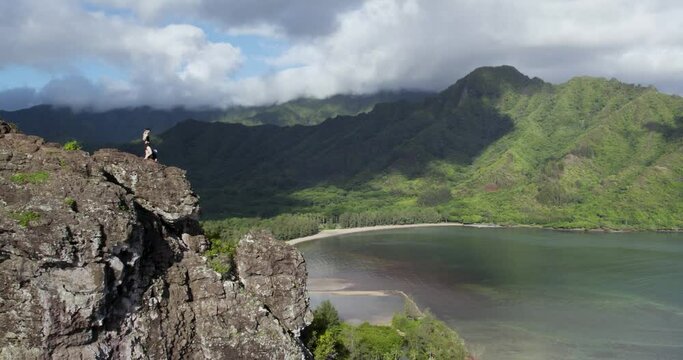 Hiker Standing On Top Of Cliff Of Crouching Lion Trail With Kahana Bay Beach Park At Summer In Oahu, Hawaii. - aerial