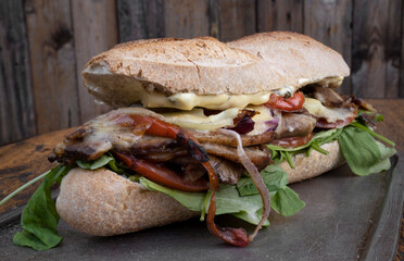 Gourmet sandwich. closeup view of a sandwich made with bread, grilled meat, arugula, cheese and onion. 