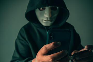 An anonymous masked hacker is using a smartphone to penetrate credit card financial information....