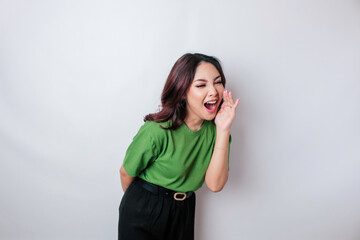 Young beautiful woman wearing a green t-shirt shouting and screaming loud with a hand on her mouth. communication concept.